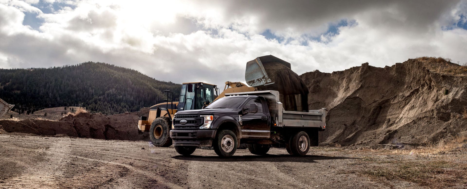 A Ford dump truck being filled with dirt by a shovel construction truck.