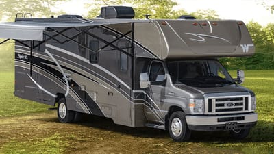 Class C motorhome built on a Ford E-Series  is parked in a large grassy field with the awening extended.